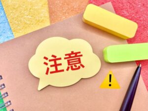 カラフルな文具に囲まれたノートの上に注意と書かれた吹き出しの付箋