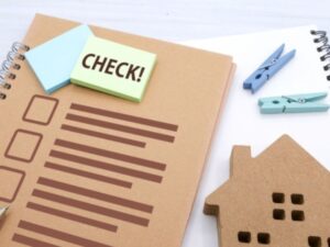 CHECKと書かれた付箋とチェックリストのノートの横に家のオブジェが置かれた住宅確認のイメージ画像